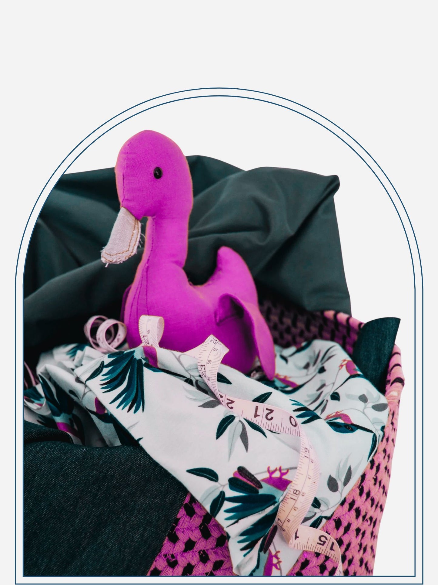 A brown linen duck toy placed in a wicker basket with various patterned fabrics and a measuring tape.