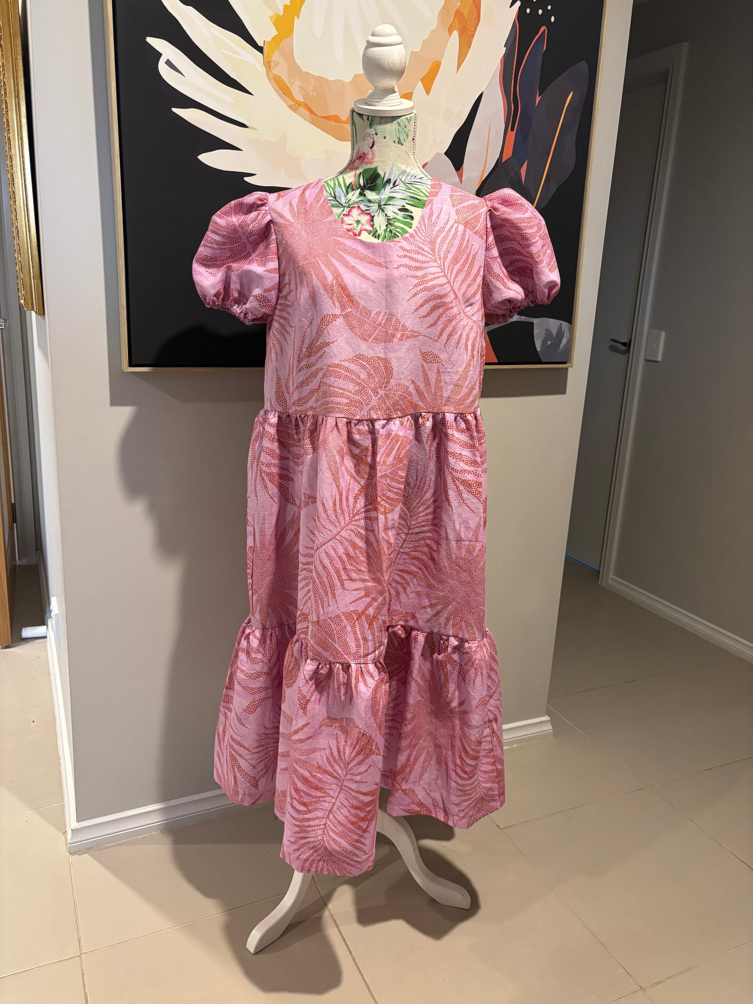 Pink floral dress on a mannequin in front of a painting