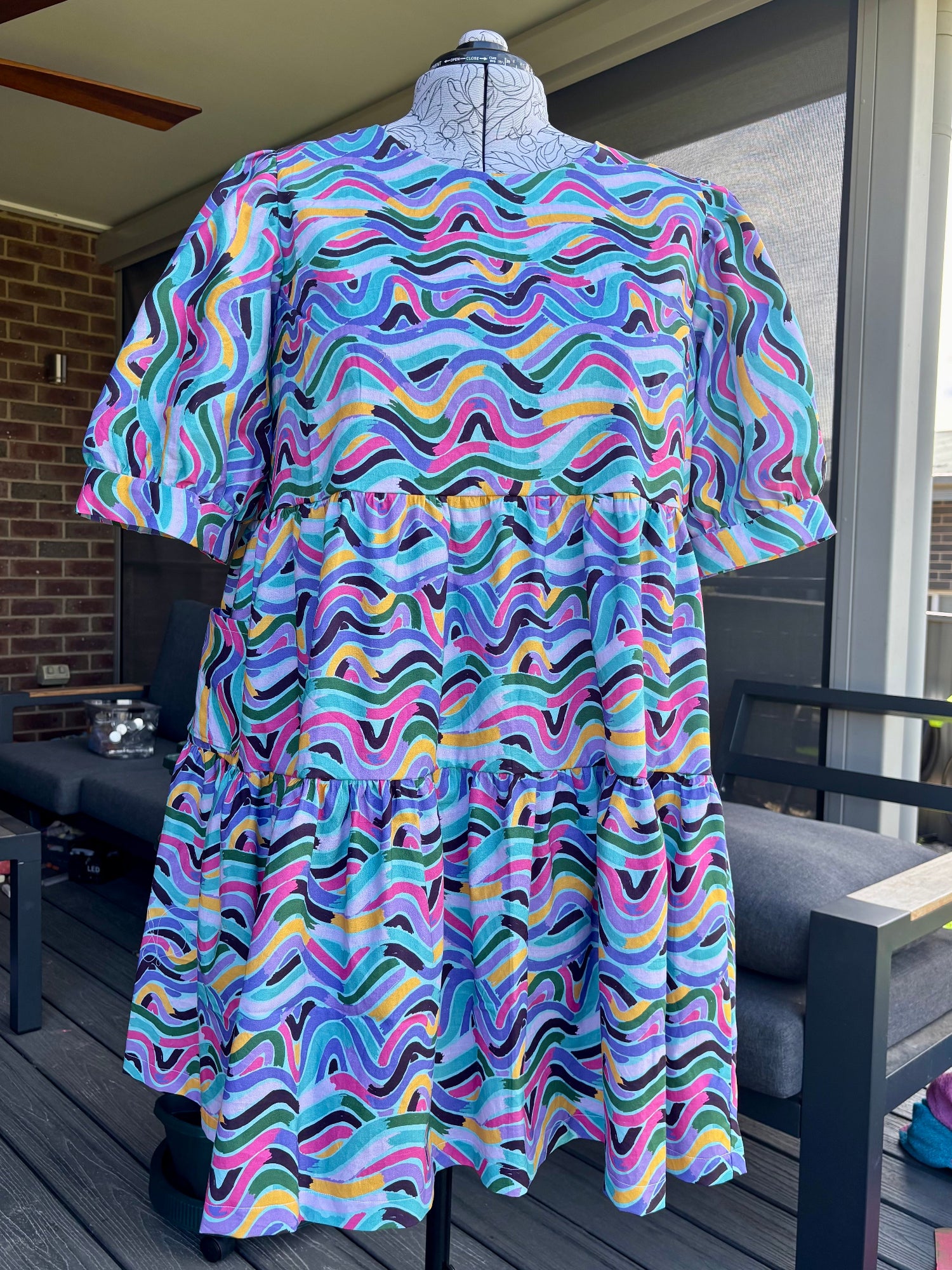 A wavy blue tiered dress displayed on a mannequin, with pockets, against an outdoor background.