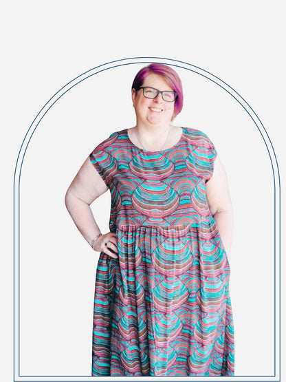 A woman standing on a deck wearing a red and black geometric patterned cap-sleeve mid-length dress.